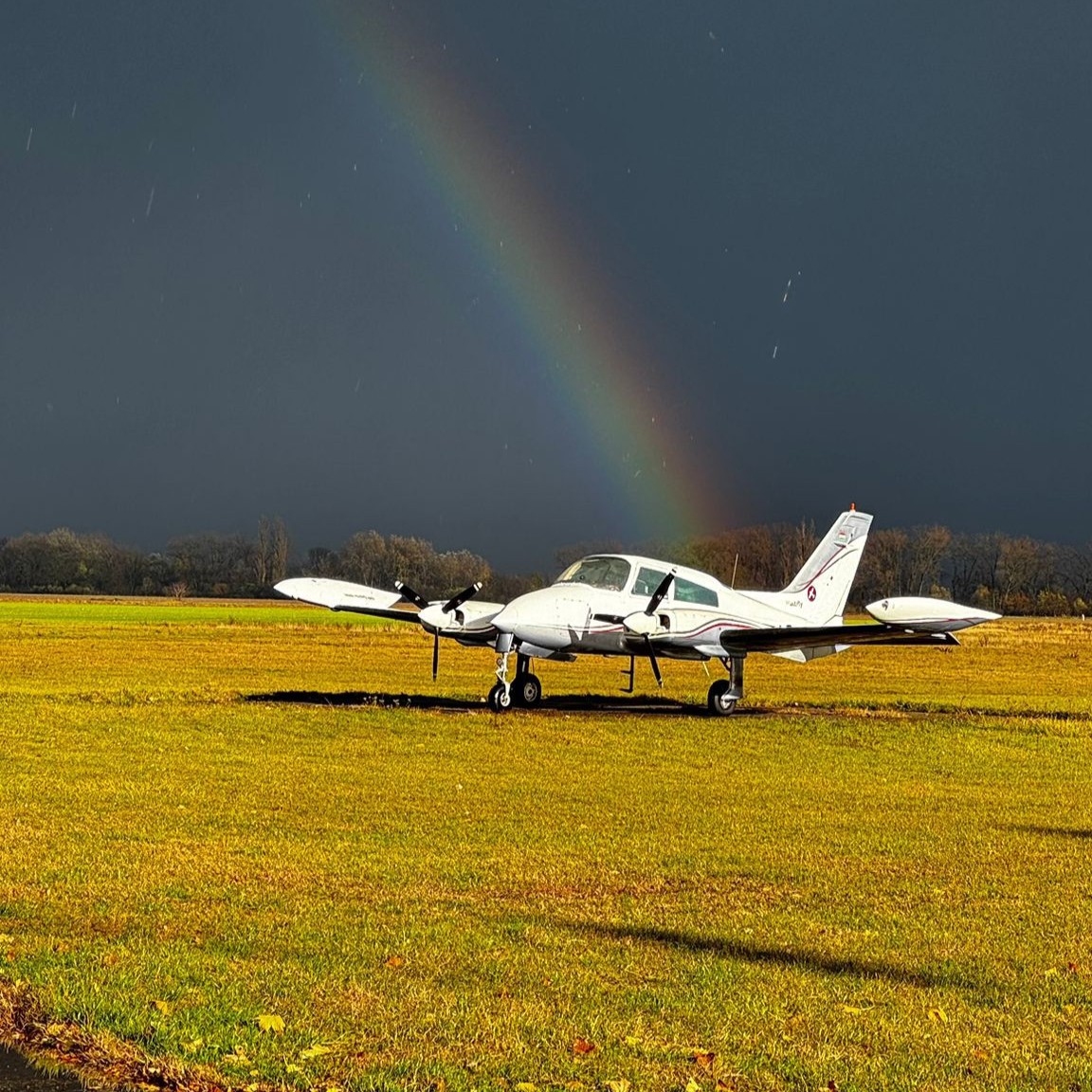 HunAviation twin-engine training aircraft on airfield with rainbow in background
